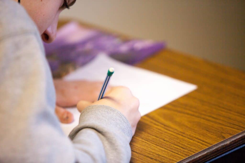 Close up of a young female writing with pencil and paper on a table.