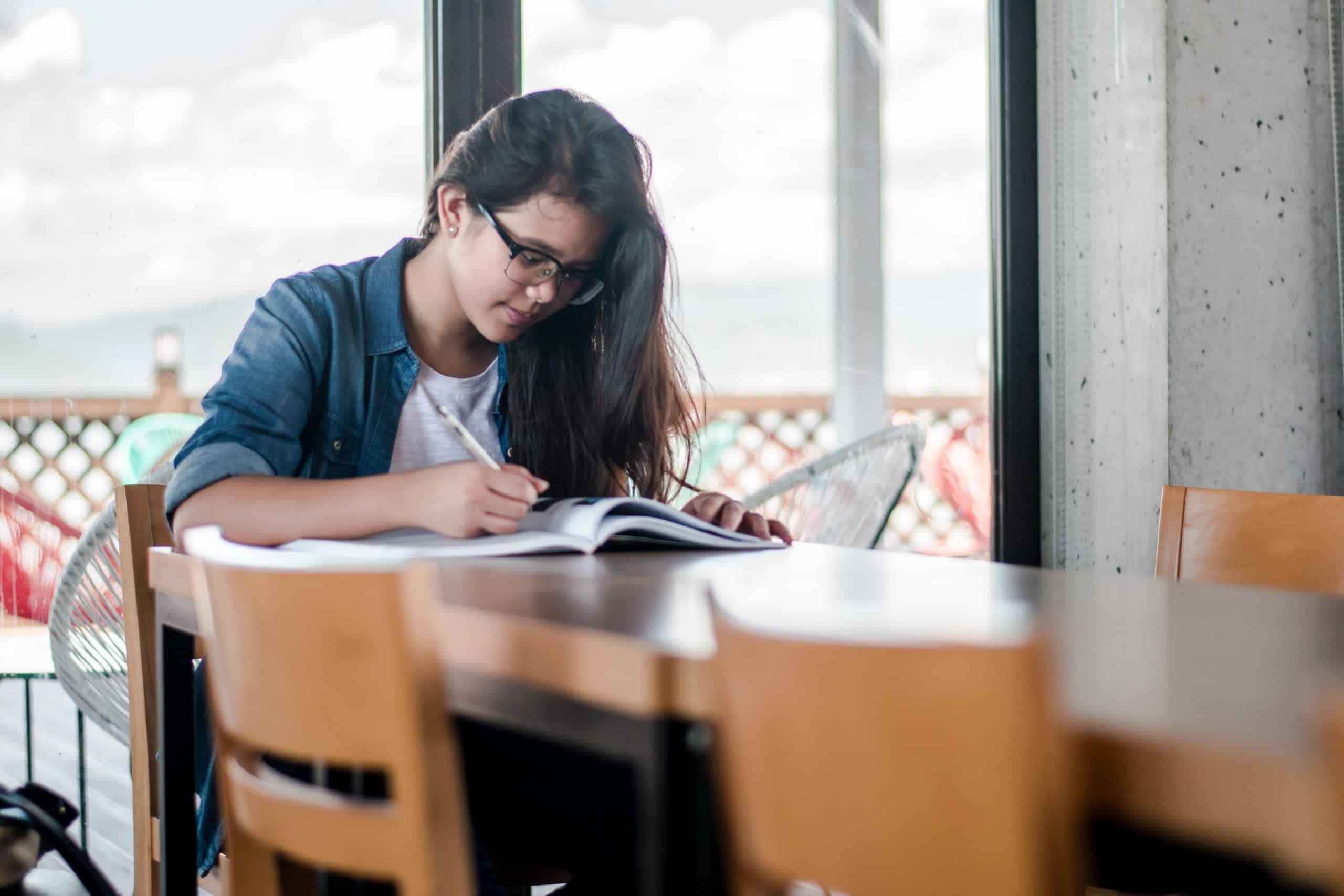 Female student studying with book and pen on a desk.
