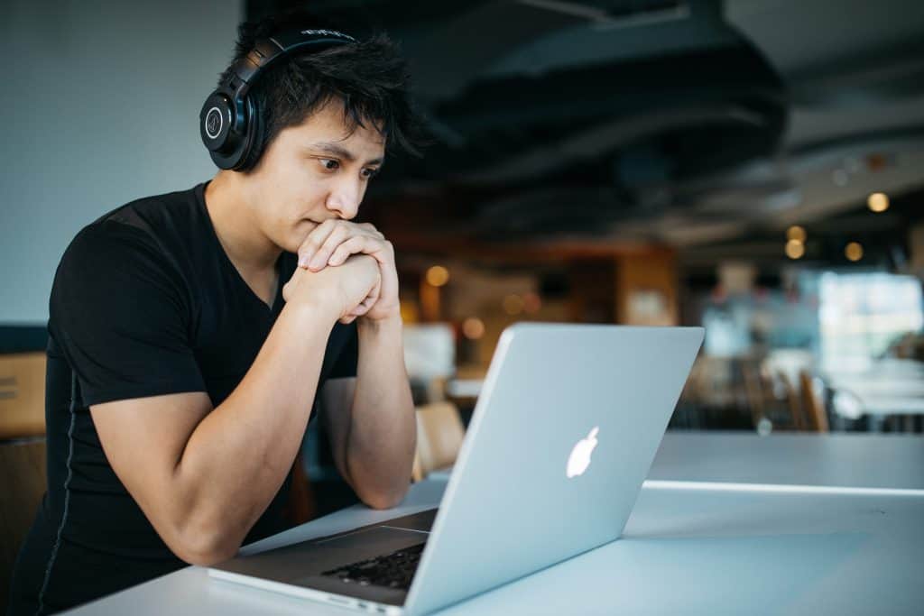 Young male sitting in front of an apple laptop with headphones on.