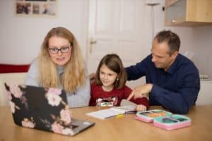 adult female, young female child and adult male looking at a laptop together.