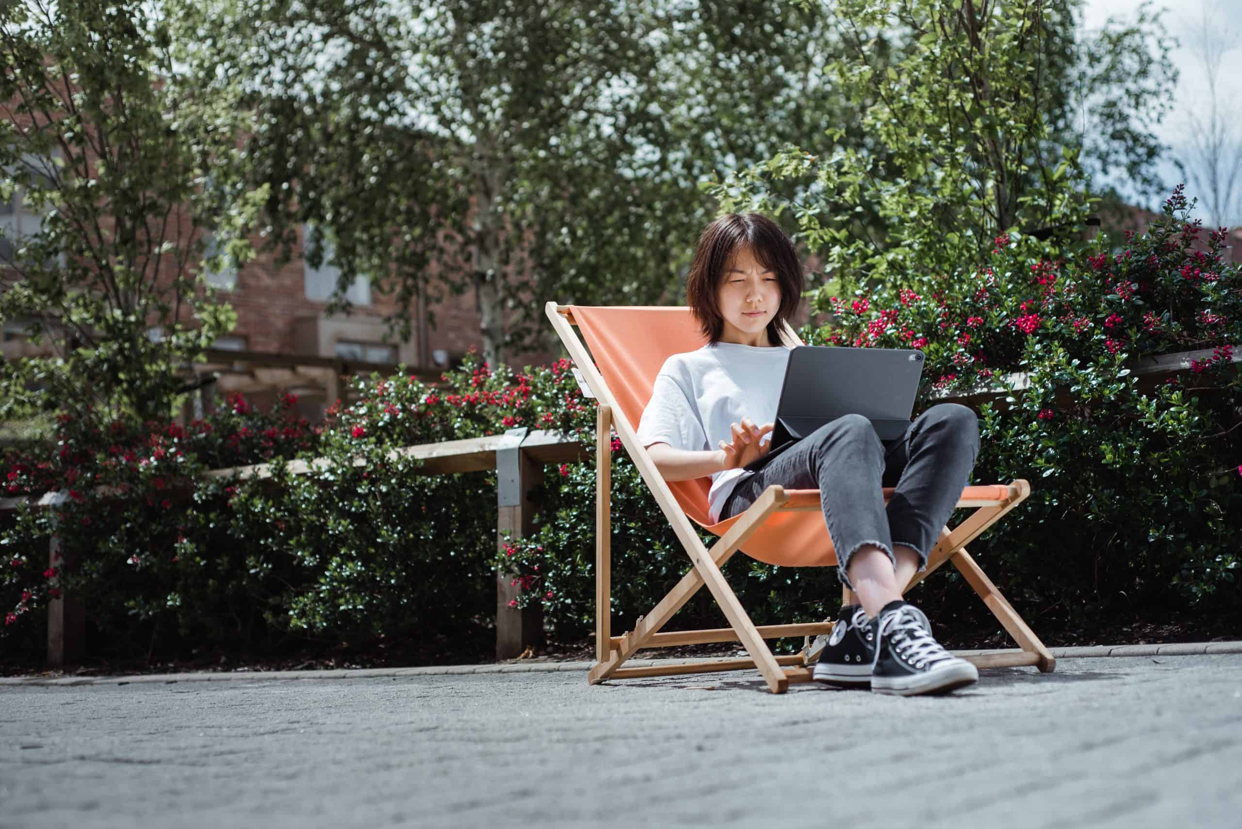 young NEC student with laptop studying outdoors as a distance learner