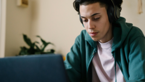 Young man wearing headphones and studying on a laptop at home, representing focused distance learning and exploring educational pathways like AS levels.