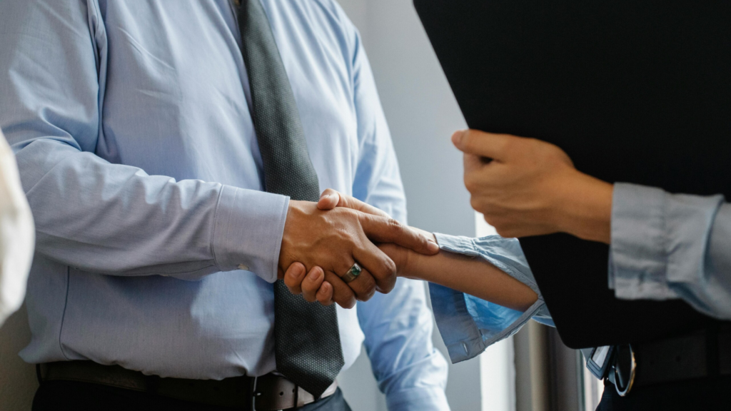 Two professionals shaking hands during a business meeting, symbolising career progression and the benefits of earning a recognised management qualification online.