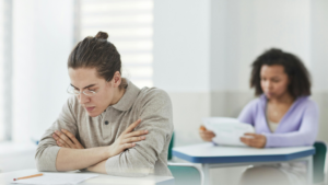 A student sitting at a desk looking focused and determined while reading an exam paper in a quiet exam hall setting.