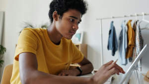 A focused teenage student using a tablet and stylus at a desk, working independently in a home environment. Casual clothing and a tidy room setting reflect a personalised and flexible home education approach.