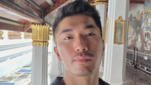 A mature student taking a selfie in a richly decorated corridor with gold accents and mural walls, representing the flexibility of studying abroad through distance learning.