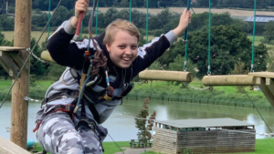 A teenage girl smiling on a high ropes adventure course, wearing a safety harness, representing the freedom and confidence that flexible homeschooling provides for ambitious young learners.