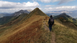 Student hiking alone on a mountain ridge path with scenic views, symbolising the independent path of online learning.