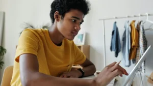 A focused teenage student using a tablet and stylus at a desk, working independently in a home environment. Casual clothing and a tidy room setting reflect a personalised and flexible home education approach.