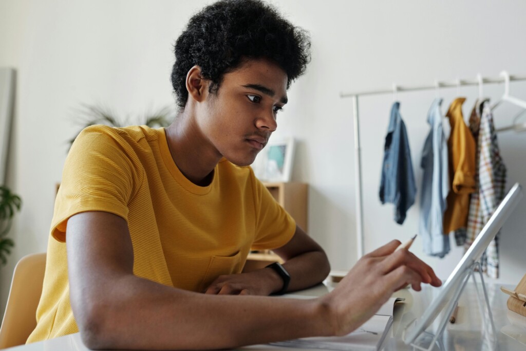 A focused teenage student using a tablet and stylus at a desk, working independently in a home environment. Casual clothing and a tidy room setting reflect a personalised and flexible home education approach.