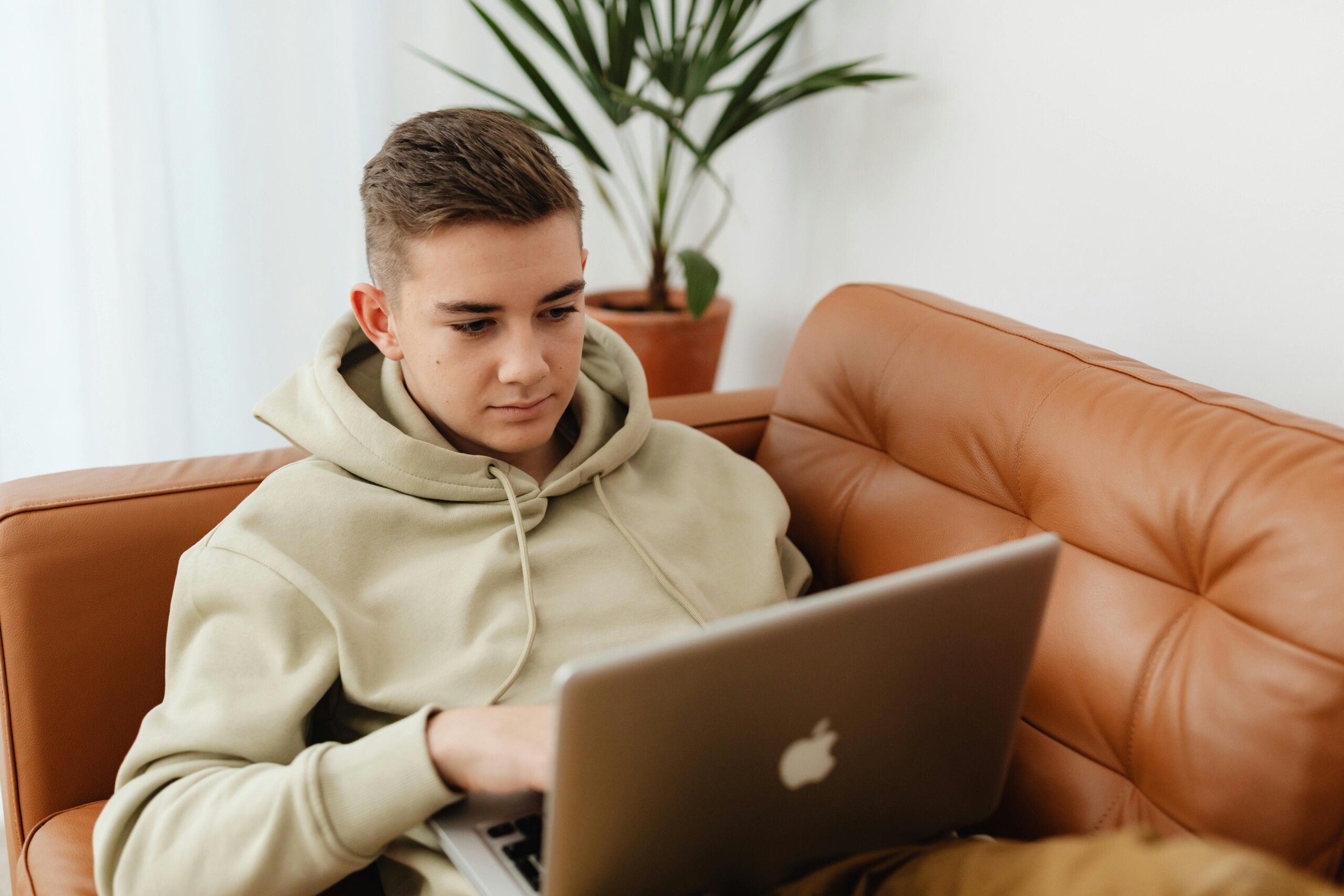 Teenage student in a hoodie studying on a laptop from a sofa, representing relaxed, flexible learning with distance education and AS level courses.