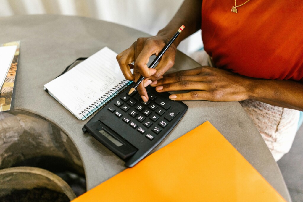 Close-up of hands using a calculator next to a notepad and orange folder, symbolising practical maths use in education, finances, and career planning.