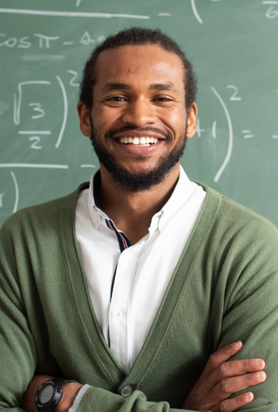 Tutor smiles into the camera with a board of mathematical equations behind him