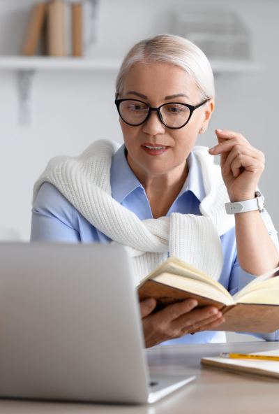 Tutor sitting at her desk with a laptop and a reference book in her hand