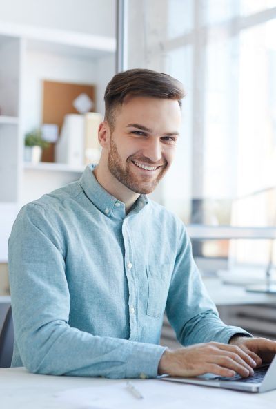 Smiling tutor sitting at his desk typing
