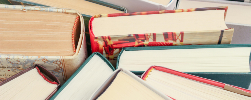 A close-up view of the tops of several stacked hardcover books with colourful bindings, representing a collection of classic and contemporary literature.