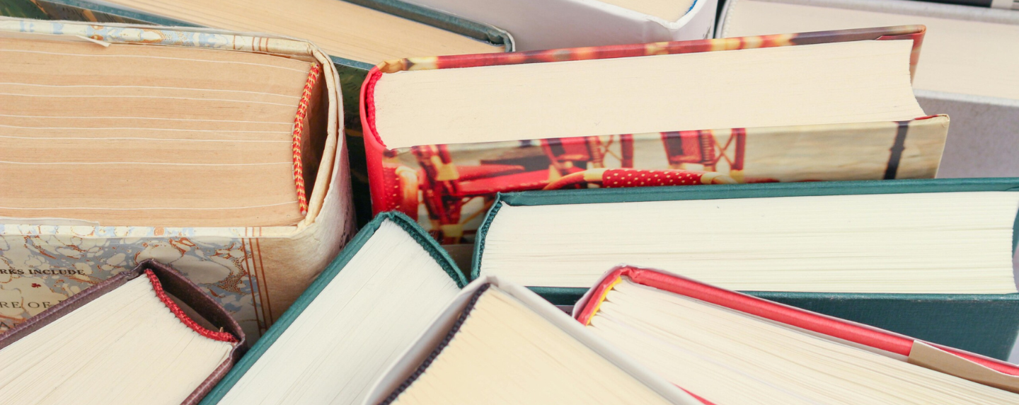 A close-up view of the tops of several stacked hardcover books with colourful bindings, representing a collection of classic and contemporary literature.