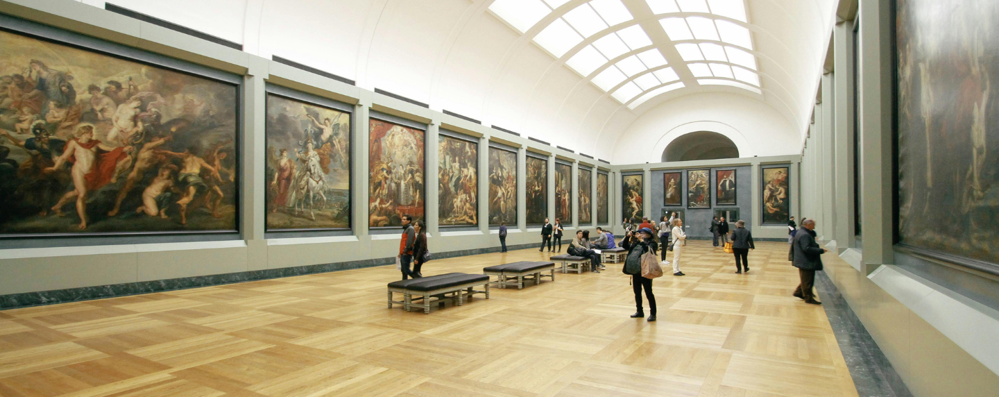 Visitors walking through an art gallery with large classical and Renaissance paintings displayed on both sides, representing the study of art history and visual culture.