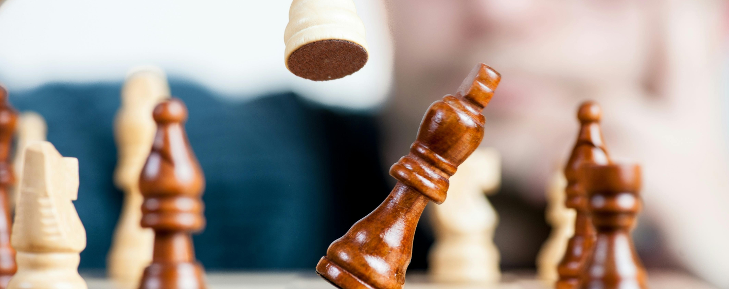 Close-up of chess pieces mid-move on a board, symbolising strategic thinking, logic, and philosophical decision-making.