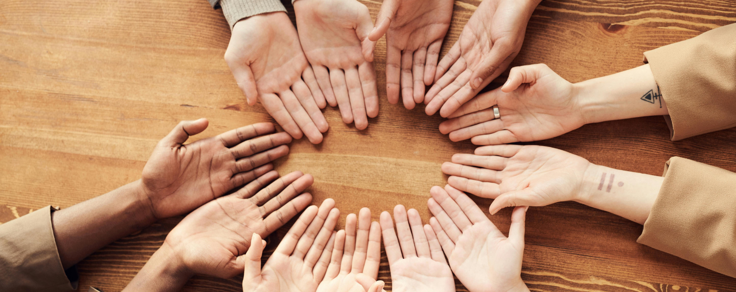A group of diverse hands arranged in a circle on a wooden table, symbolising unity, inclusion, and social connection—key themes in sociology.
