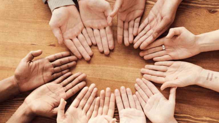 A group of diverse hands arranged in a circle on a wooden table, symbolising unity, inclusion, and social connection—key themes in sociology.