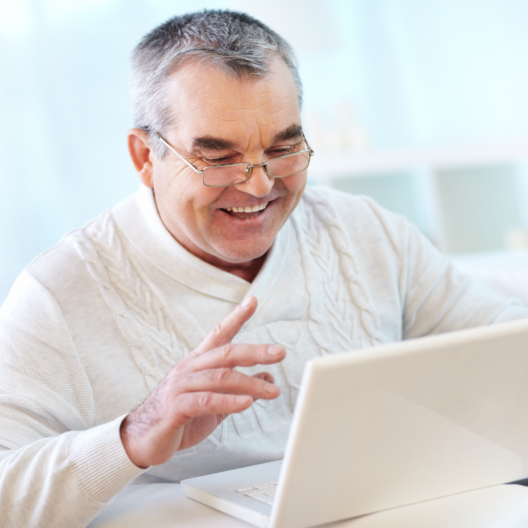 Older man sits smiling at something on his laptop