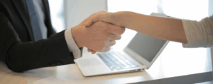 Two people shaking hands over a laptop, symbolising business agreements, partnership, and professional communication.