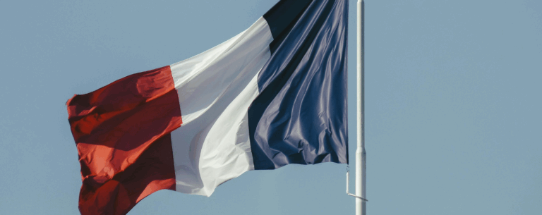 The French flag waving against a clear sky, symbolising the study of French language and culture.