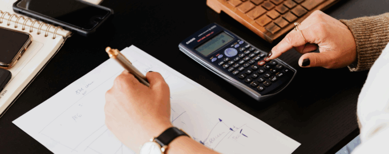A person using a scientific calculator and writing mathematical graphs on paper, representing advanced maths problem-solving.