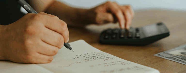A person writing calculations in a notebook while using a calculator, representing mathematical thinking and problem-solving.