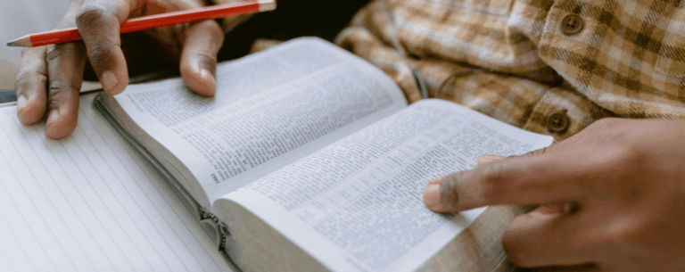 A person reading a text and making notes with a pencil, symbolising the academic study of religion, ethics, and philosophy.