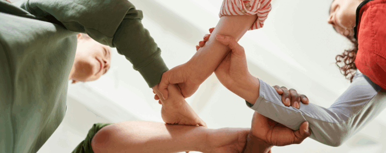 A group of people holding each other's arms in a supportive circle, symbolising social bonds, community, and human relationships.