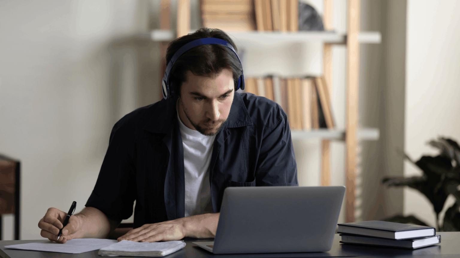 Business management online courses with the NEC. Man sat at desk with headphones on studying with a laptop