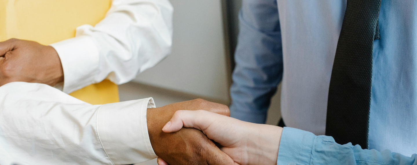 Close-up of diverse professionals shaking hands in a workplace setting, representing leadership, teamwork, and management development.