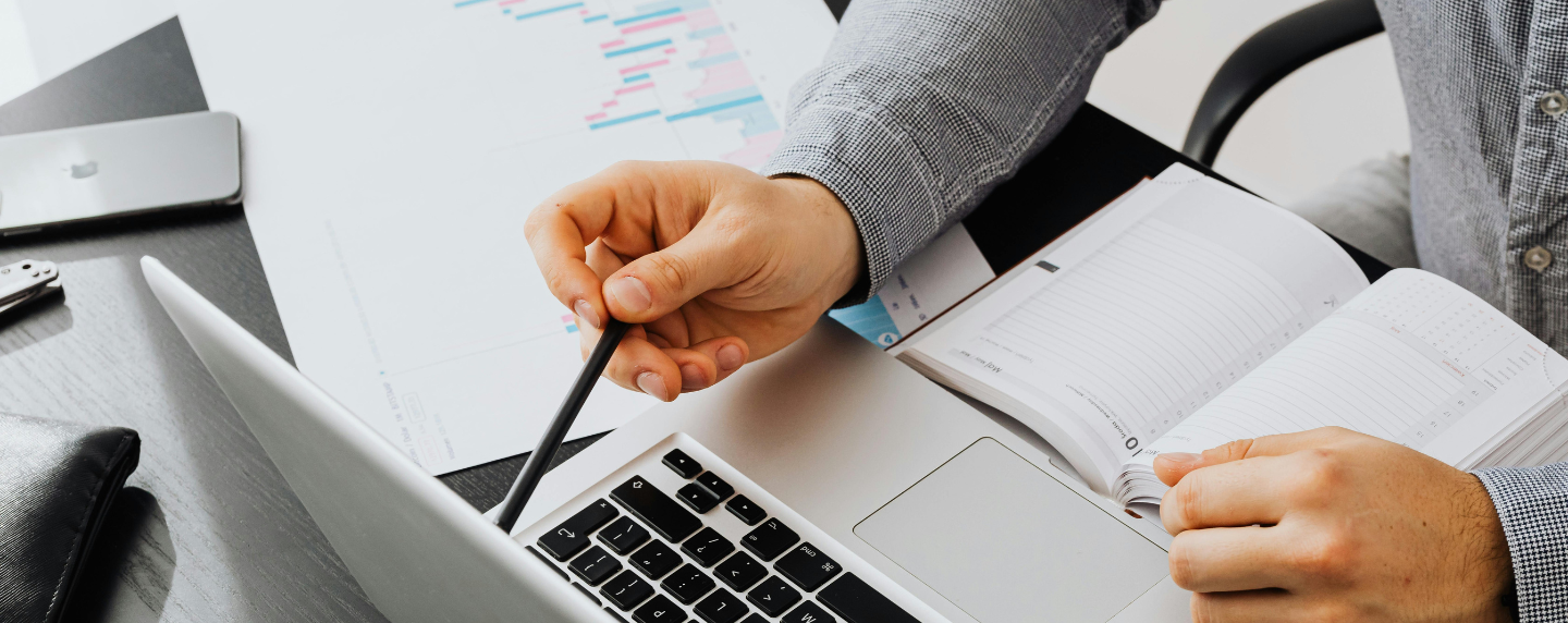 Close-up of a manager reviewing a laptop and charts while discussing strategy and planning using a pen and a notebook.