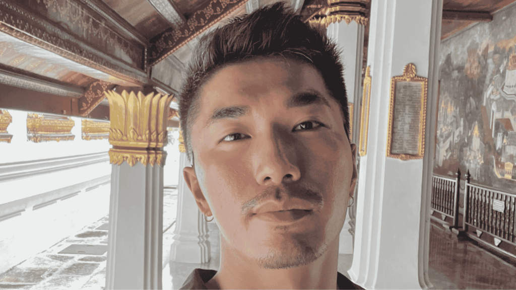A mature student taking a selfie in a richly decorated corridor with gold accents and mural walls, representing the flexibility of studying abroad through distance learning.