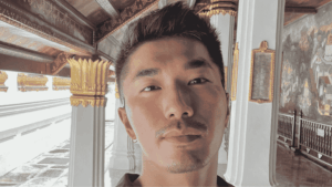 A mature student taking a selfie in a richly decorated corridor with gold accents and mural walls, representing the flexibility of studying abroad through distance learning.