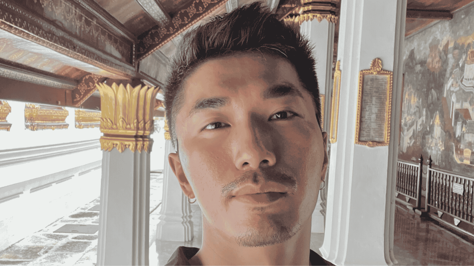 A mature student taking a selfie in a richly decorated corridor with gold accents and mural walls, representing the flexibility of studying abroad through distance learning.