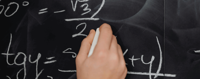 Close-up of a student’s hand solving trigonometric and algebraic equations on a chalkboard, symbolising advanced mathematics learning.