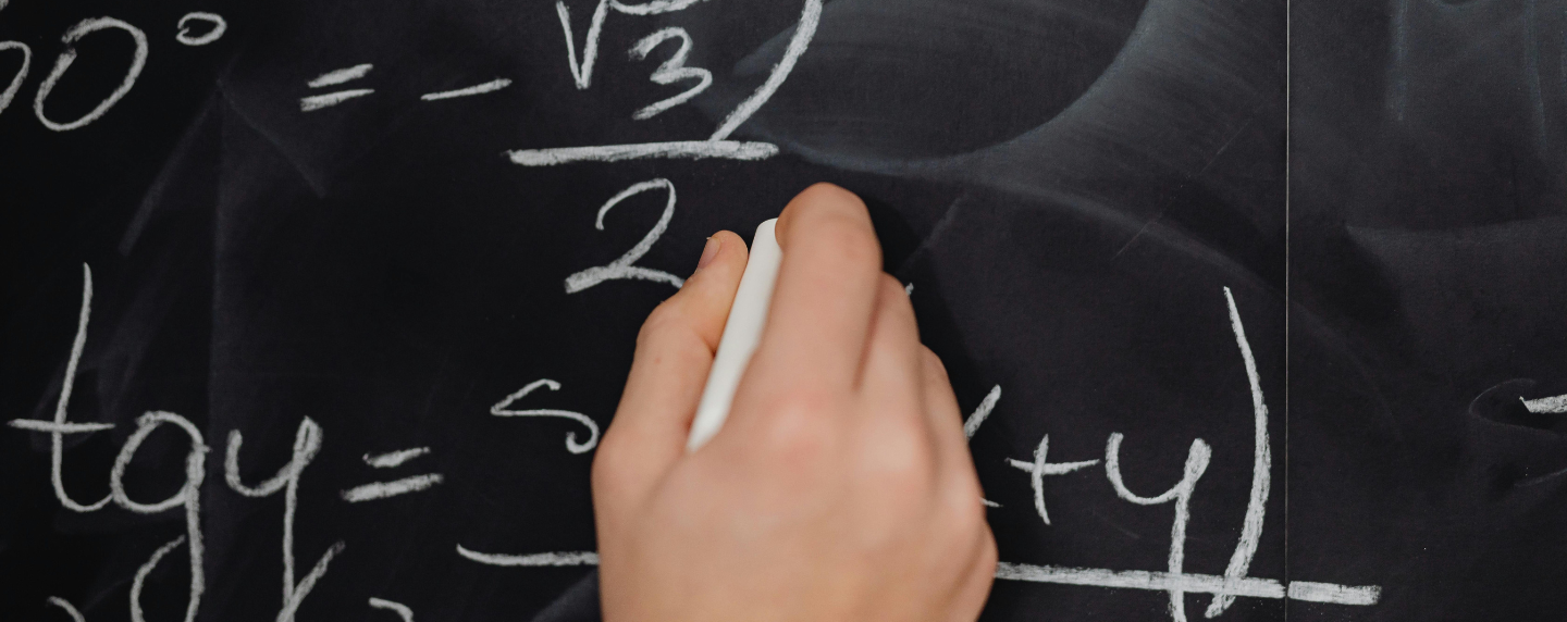 Close-up of a student’s hand solving trigonometric and algebraic equations on a chalkboard, symbolising advanced mathematics learning.