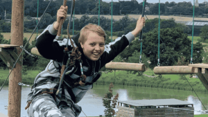 A teenage girl smiling on a high ropes adventure course, wearing a safety harness, representing the freedom and confidence that flexible homeschooling provides for ambitious young learners.