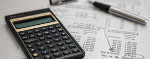 Close-up of a calculator and financial documents used in bookkeeping, alongside a pen and handwritten notes.