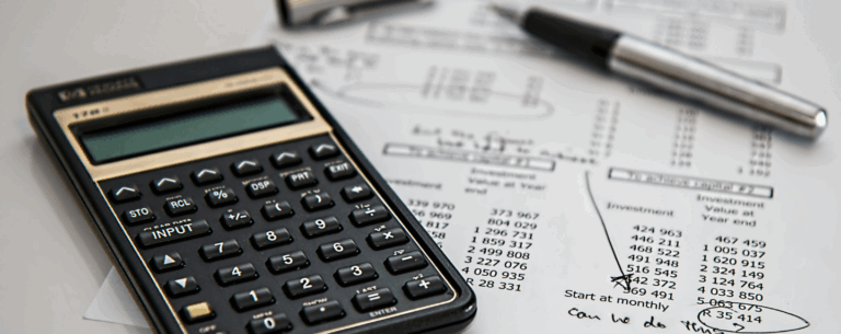 Close-up of a calculator and financial documents used in bookkeeping, alongside a pen and handwritten notes.