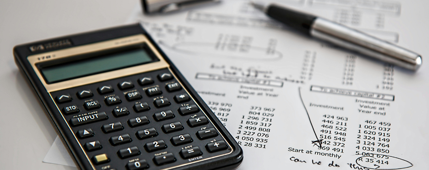 Close-up of a calculator and financial documents used in bookkeeping, alongside a pen and handwritten notes.