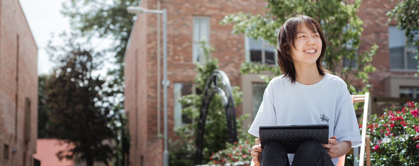 A smiling student studying outside with a tablet, representing flexible online learning for international A level students