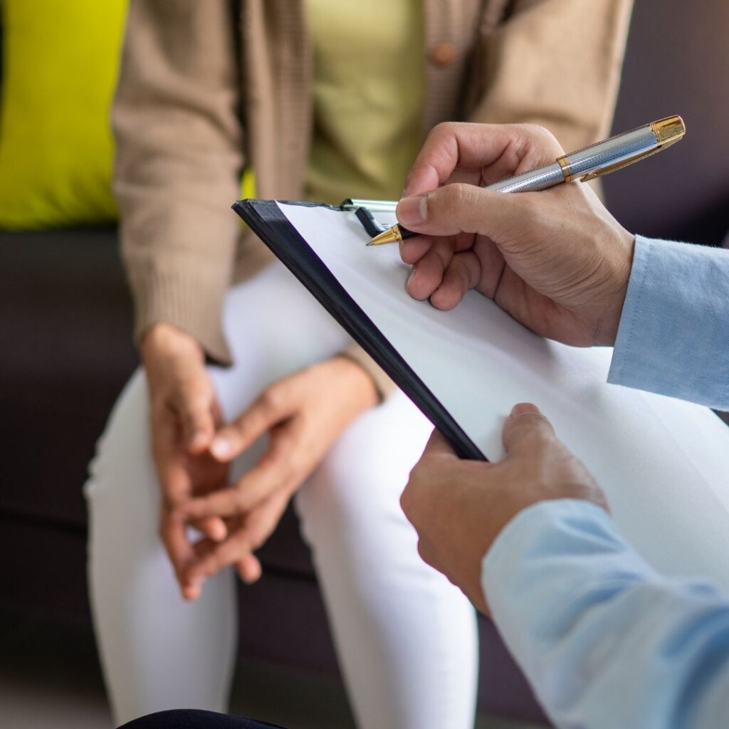 Online counselling courses with the NEC. Two people on chairs talking to each other, on in a blue shirt is taking notes, this is a close up image of their hands.