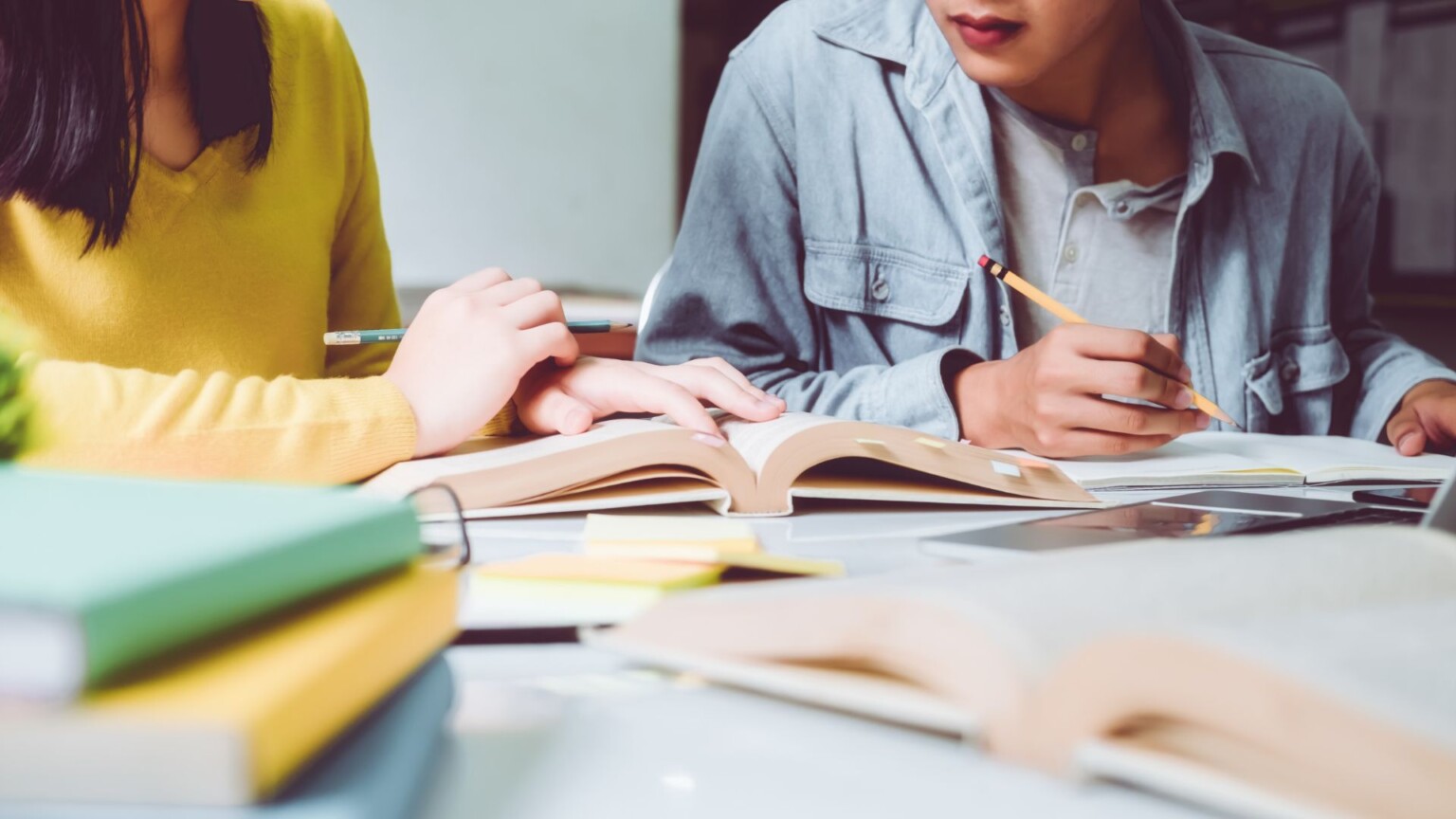 Online teaching courses. Two females at a desk pouring over books studying.