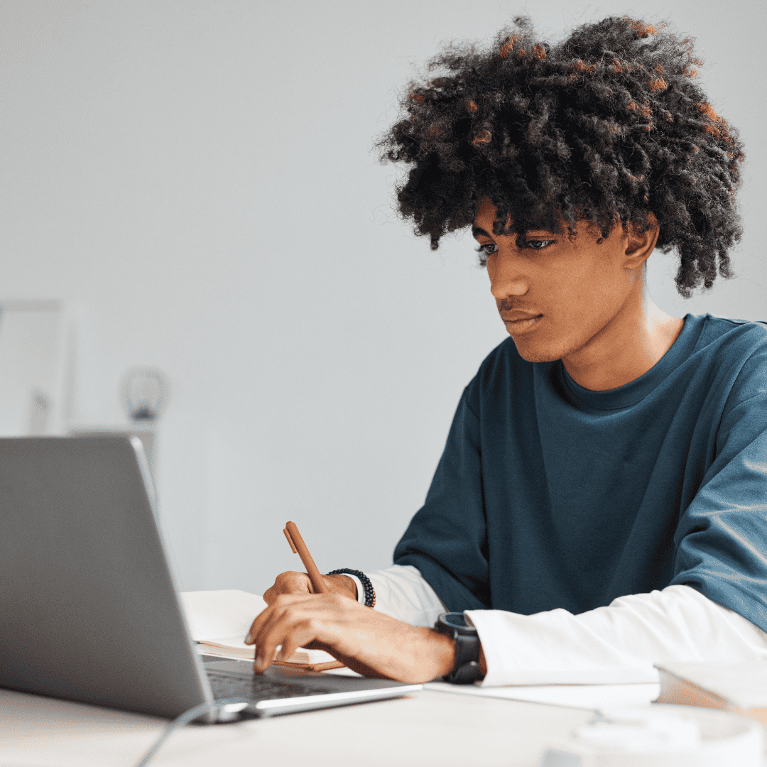 Teenage boy with an impressive afro haircut is concentrating hard as he sits studying at home on his laptop