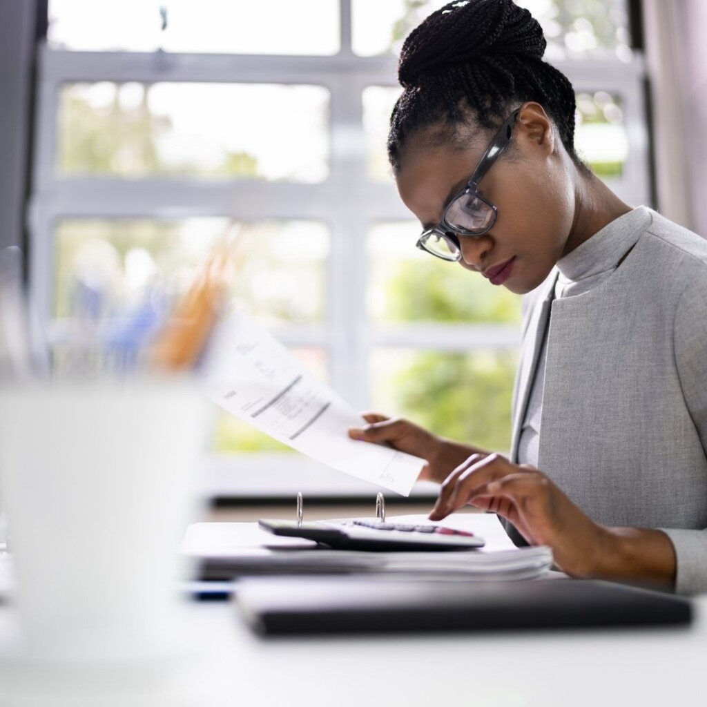 Vocational qualifications with NEC. Woman sat at a desk look over paperwork with a calculator.