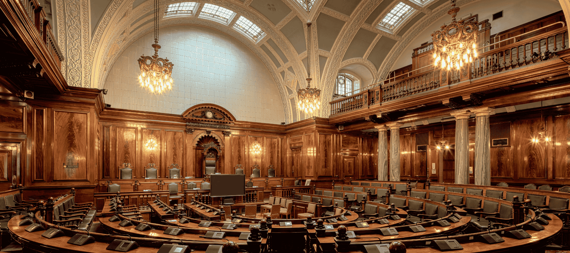 An ornate parliamentary chamber with wooden benches and chandeliers, symbolising political debate, governance and democracy.